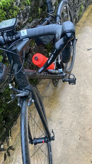 A road bike leaning against a wall. The front shifter is stuck inwards at an awkward angle